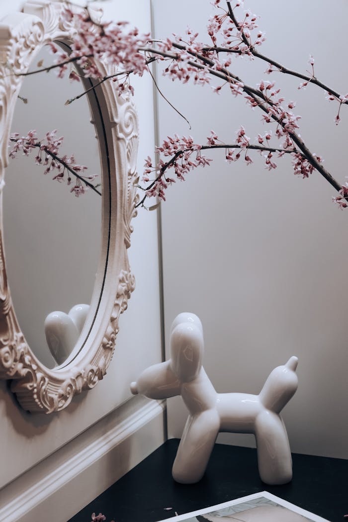 A decorative mirror reflects branches and a ceramic poodle in an elegant home setting.